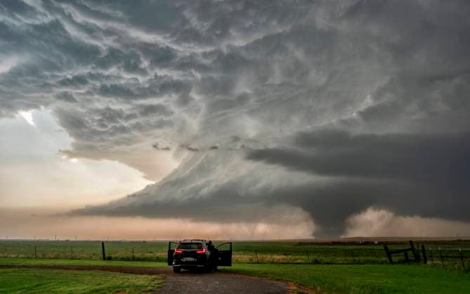 A storm chaser s vehicle parked on a dirt road observing a massive tornado forming under a dark, dramatic sky in an open field. Olustee, Oklahoma United States peja00028 Copyright: xConnectxImagesx