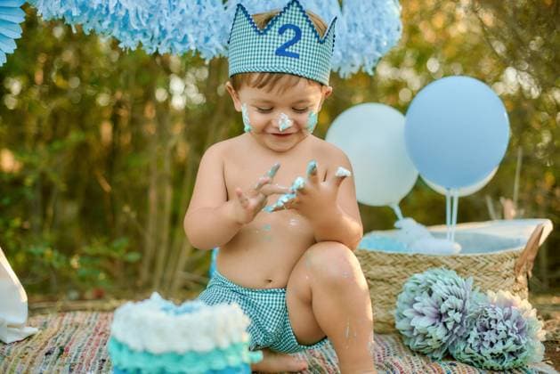 Creative Highlights Symbolbilder A joyful toddler wearing a blue and white crown enjoys a cake smash during his second birthday celebration outdoors, surrounded by balloons and flowers Model Released GAEED9~1 Copyright: xx