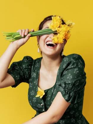 Creative Highlights Symbolbilder A cheerful woman in a green floral dress covers her eyes with a bunch of fresh yellow daffodils, laughing against a vibrant yellow background Model Released KateSurzhok_ID15262_465699_002 Copyright: xKatexSurzhokx