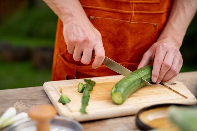 Close up of man holding sharp knife, peeling cucumber. Preparing vegetables for an outdoor barbecue. Close up of man holding sharp knife, peeling salad cucumber. Preparing vegetables for an outdoor barbecue. model released