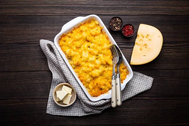 Nahaufnahme von gebackenen Maccaroni und Käse in weißer Kasserolle auf rustikalem Holzhintergrund, mit Gewürzen, Butter, Löffel und Gabel, Ansicht von oben. Nudeln mit Käsesauce, amerikanische englische Hausmannskost Close-up of baked mac and cheese in white casserole on rustic wooden background, with seasonings, butter, spoon and fork, top view. Pasta with cheesy sauce, American English comfort food Copyright: imageBROKER OlenaxYeromenko ibliqx08591090.jpg