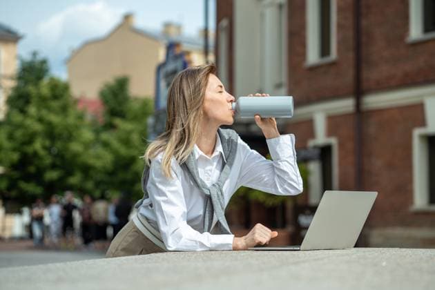 IMAGO Creative, Jahreszeit Sommer, Hitze Happy woman with laptop outside drinking water from bottle, coping with dehydration, thirst. Businesslike girl using computer, working outside, enjoying fresh air, warm weather. Satisfied smiling woman replenishes balance of fluids in body by drinking water with pleasure at hot summer day. ,model released, Symbolfoto Copyright: xZoonar.com DmitriixMarchenkox 22036083 ,model released, Symbolfoto ,property released