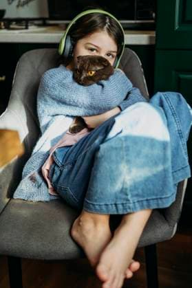 Creative Highlights Symbolbilder Girl wearing wireless headphones embracing cat and sitting on chair at home model released, Symbolfoto property released, ANAF03508