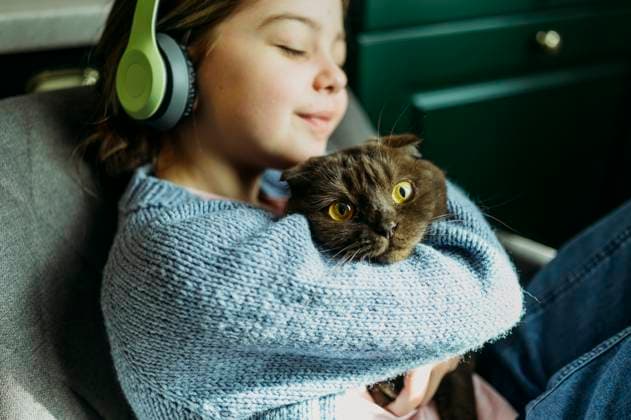 Girl wearing wireless headphones with eyes closed embracing cat at home model released, Symbolfoto property released, ANAF03509