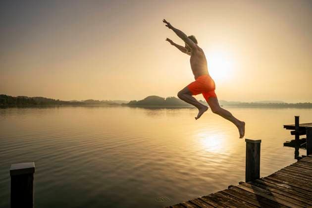 Creative Highlights Symbolbilder Active senior jumping in lake at sunrise model released, Symbolfoto, DIGF21631