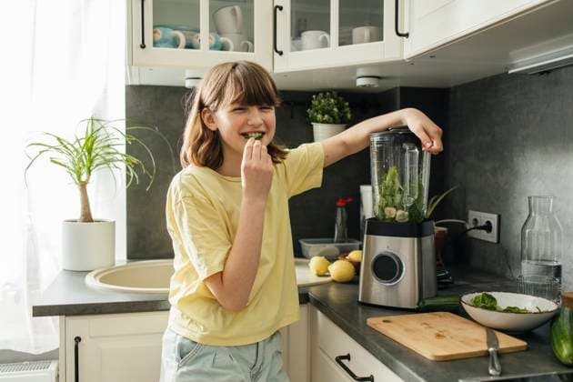 Smiling girl eating spinach leaf and making smoothie in kitchen at home model released, Symbolfoto property released, ELMF00669