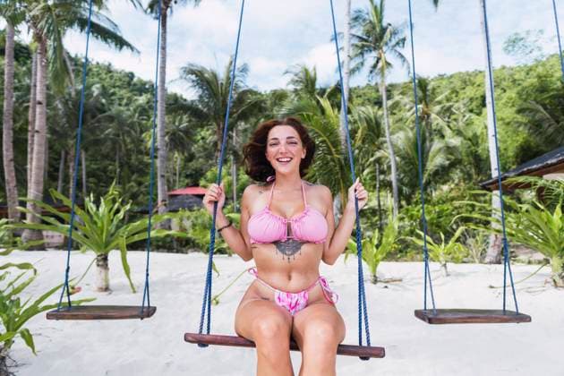 Creative Highlights Symbolbilder Smiling young woman in swimwear sitting on swing at beach model released, Symbolfoto property released, PNAF06482