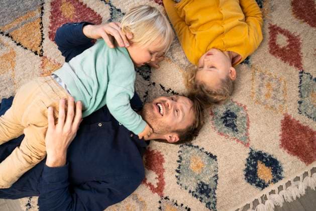Smiling father lying down with son and daughter on carpet at home model released, Symbolfoto property released, SBOF04186