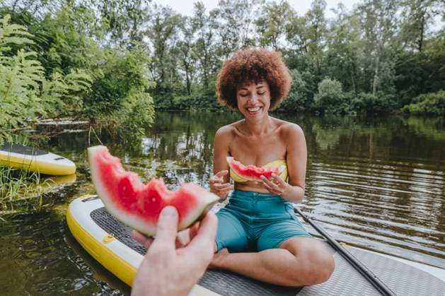 Happy woman eating watermelon with friend on paddleboard in lake model released, Symbolfoto, YTF01036