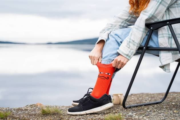 Creative Highlights Symbolbilder A person wearing casual clothes and orange socks sits relaxed by a serene lake, exemplifying the peaceful experience of outdoor camping Model Released AlbaVitta_ID18978_564952_025 Copyright: xAlbaxVittax RECORD DATE NOT STATED