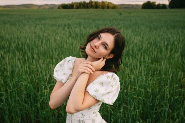 Creative Highlights Symbolbilder A young woman stands gracefully in a lush field, dressed in a white floral prom dress Her engaging smile and serene pose capture a moment of youthful elegance amid the expansive natural landscape Model Released CamilleGirard_ID13413_408632_017 Copyright: xCamillexGirardx