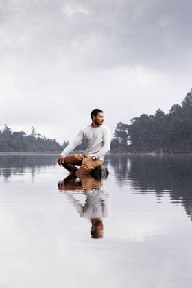Creative Highlights Symbolbilder A contemplative latin man sits serenely on a calm, reflective lake surface under a cloudy sky, symbolizing peace and reflection Model Released EduardoGavira_ID23395_679851_009 Copyright: xEduardoxGavirax RECORD DATE NOT STATED