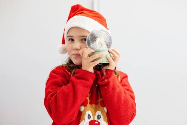 Creative Highlights Symbolbilder A young girl, wearing a Santa hat and a festive red sweater with a reindeer design, gazes at a Christmas-themed snow globe she is holding Model Released HodeiUnzueta_ID23536_683559_040 Copyright: xHodeixUnzuetax