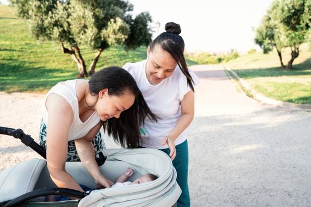 IMAGO Creative, Diversity, Familie: Gleichgeschlechtliche Eltern: Zwei Mütter A loving lesbian couple smiles as they interact with their infant son in a stroller during a stroll in the park on a sunny day Model Released ManuelRuiz_ID23737_688745_065 Copyright: xManuelxRuizx