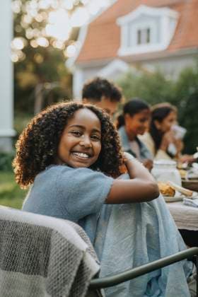 IMAGO Creative, Lifestyle, Feste im Garten #2 Portrait of happy curly hair girl sitting on chair at social gathering in back yard Sweden, Gothenburg, model released, property released Copyright: xMaskotx, MA111558