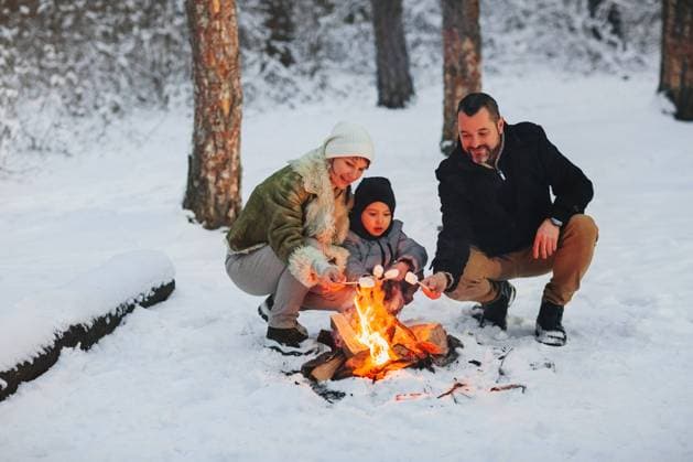 Fröhliche Eltern und Sohn genießen ein heißes Getränk, während sie sich abends am Lagerfeuer im Winterwald ausruhen Cheerful parents and son enjoying hot drink while resting near campfire in evening in winter forest Copyright: imageBROKER DashaxPetrenko ibxiqx09196095.jpg ,model released, Symbolfoto ,property released