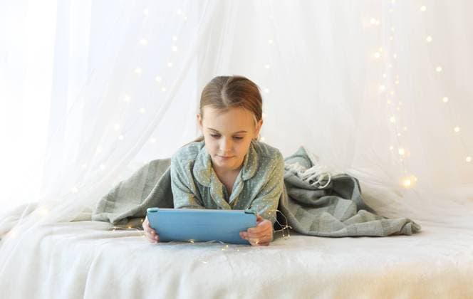 IMAGO Creative, Weihnachten, Tradition: Weihnachtsfilme sehen Kinder und moderne Technologien. Kleines Mädchen im Pyjama liegend mit modernen digitalen Tablette auf Baldachin Prinzessin Bett mit gelben Lichtern Weihnachten dekoriert, Kind gerade Filme oder Cartoons am Weihnachtsmorgen Children and modern technologies. Little girl lying in pajama with modern digital tablet on canopy princess bed decorated with yellow xmas lights, kid watching movies or cartoons on Christmas morning Copyright: imageBROKER DashaxPetrenko ibxiqx09198443.jpg ,model released, Symbolfoto ,property released