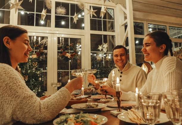 Ein glückliches Familienpaar stößt mit Sektgläsern an, während es Silvester oder Weihnachten mit Freunden feiert und an einem festlich gedeckten Tisch mit traditionellen Speisen und brennenden Kerzen sitzt Happy family couple clinking champagne glasses while celebrating New Years Eve or Christmas with friends, sitting at festive dinner table with traditional food and burning candles Copyright: imageBROKER DashaxPetrenko ibxiqx09201343.jpg ,model released, Symbolfoto ,property released