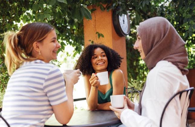 Multiethnische Gruppe von Mädchen in Freizeitkleidung und traditionellem Hijab, die sich im Freien unterhalten und Spaß haben. Drei junge Teenagermädchen in einem Gartencafé trinken Tee oder Kaffee Multiethnic group of girls wearing casual clothes and traditional hijab bonding and having fun outdoors. Three young teen girls in garden cafe drinking tea or coffee Copyright: imageBROKER DashaxPetrenko ibxiqx09201379.jpg ,model released, Symbolfoto ,property released