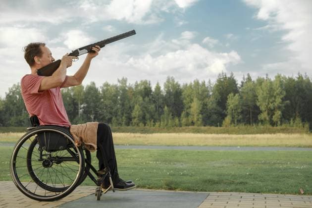 Älterer Mann mit gelähmten Beinen im Rollstuhl zielt mit einer doppelläufigen Flinte auf einem Schießstand im Freien Senior man with paralysed legs in wheelchair aiming double-barreled shotgun at an outdoor shooting range Copyright: imageBROKER AlekseixIsachenko ibxfbm11288360.jpg ,model released, Symbolfoto ,property released