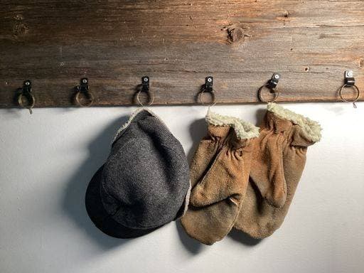 A rustic wooden coat rack with metal hooks holding a grey cap and a pair of brown mittens with white fur lining. 25735320 RECORD DATE NOT STATED