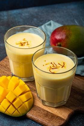 Gesundes indisches Ayurveda-Getränk Mango Lassi in zwei Gläsern auf rustikalem Betontisch mit frischer, reif geschnittener Mango, gelbes Mischgetränk aus Mangofrucht, Joghurt oder Milchquark und Gewürzen Healthy Indian Ayurveda drink mango lassi in two glasses on rustic concrete table with fresh ripe cut mango, yellow blended beverage made of mango fruit, yoghurt or milk curd and spices Copyright: imageBROKER OlenaxYeromenko ibxiqx08607739.jpg