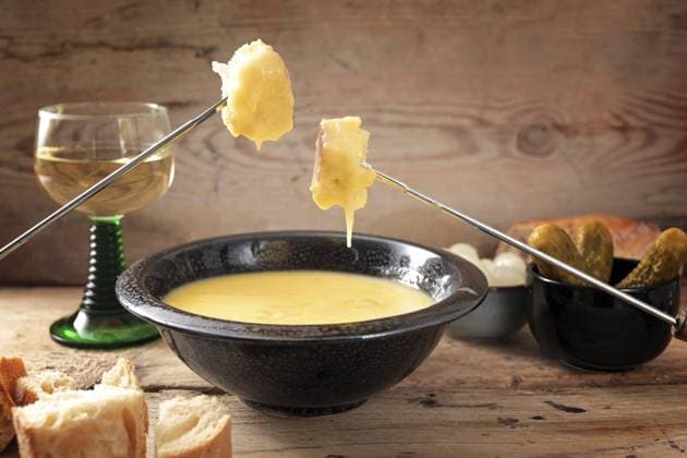 Schweizer Fondue aus geschmolzenem Käse mit Brot auf langen Gabeln, Essiggurken und Wein auf rustikalen Holzbrettern, Kopierraum, gewählter Fokus, enge Tiefenschärfe Swiss fondue from melted cheese with bread on long forks, pickles and wine on rustic wooden planks, copy space, selected focus, narrow depth of field Copyright: imageBROKER MarenxWinter ibxiqx11039356.jpg