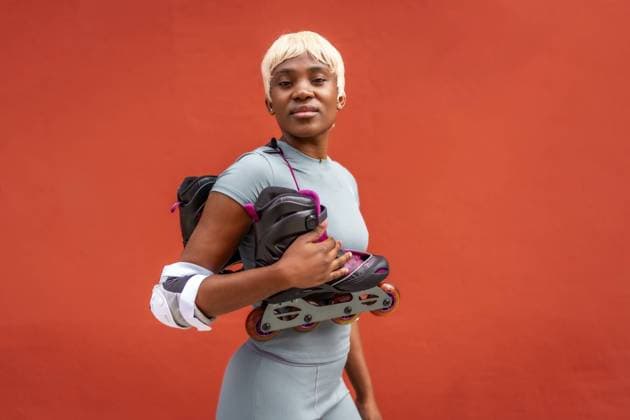 Creative Highlights Symbolfotos Urbane afrikanische Frau mit kurzen blonden Haaren trägt Inline Skates vor rotem Hintergrund Urban african woman whit short blonde hair carrying inline skates against red background Copyright: imageBROKER UnaixHuizi ibxuhu11359877.jpg ,model released, Symbolfoto ,property released