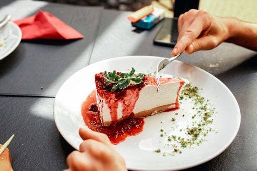 A person enjoying a slice of cheesecake with strawberry sauce at a restaurant 25213690 RECORD DATE NOT STATED