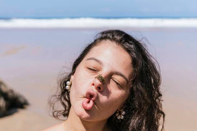 Creative Highlights Symbolfotos A playful young woman makes a funny face with a crab on her nose, on a sunny beach day, capturing a moment of joy and carefree spirit Model Released PaulaBerezo_ID23862_692517_006 Copyright: xPaulaxBerezox