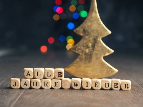 Wooden cube with the German inscription Every year again, christmas concept background with blurred Christmas lights