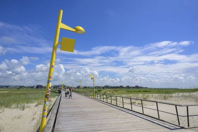 Eine holzgeplankte Promenade führt entlang eines Strandes unter einem klaren blauen Himmel mit Wolken, Sankt Peter Ording, Schleswig Holstein, Deutschland, Europa A wooden-planked promenade leads along a beach under a clear blue sky with clouds, Sankt Peter Ording, Schleswig Holstein, Germany, Europe Copyright: imageBROKER MarcusxSiebert ibxmcs11439195.jpg