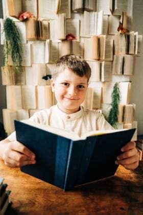 Creative Highlights Symbolfotos Smiling boy holding a blue book, wall of books behind him North Andover, Massachusetts, United States CR_FKNH240904-1527195-01 ,model released, Symbolfoto