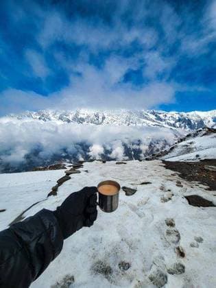 A person holding a cup of hot beverage in a snowy mountain landscape under a clear blue sky. 26144257 RECORD DATE NOT STATED
