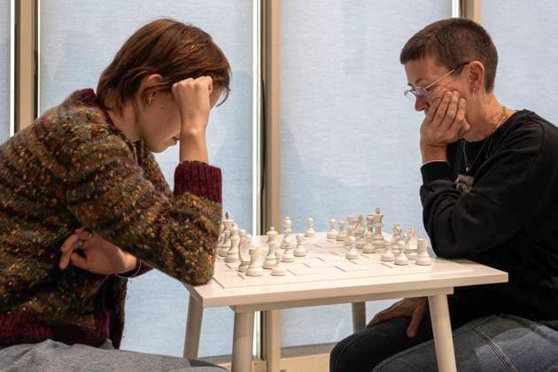 Einzelausstellung Music of the Mind von Yoko Ono in Düsseldorf. White Chess Set Play it Trust, ein weißes Schachspiel aus dem Jahr 1966. Zwei Besucherinnen der Ausstellung versuchen, zu spielen und einander zu vertrauen. Im Übrigen bezeichnen K20 und K21 der Stiftung Kunstsammlung Nordrhein-Westfalen in Düsseldorf Kunst des 20. und des 21. Jahrhunderts. Bei Yoko Ono ist s beides. Düsseldorf Nordrhein-Westfalen Deutschland