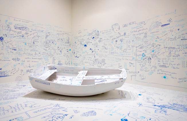 Einzelausstellung Music of the Mind von Yoko Ono in Düsseldorf. Add Colour - Refugee Boat ( Füge Farbe hinzu - Füchtlingsboot ), ein Holzboot, weiß angestrichen, wie auch der gesamte Raum weiß angestrichen ist. Es wird darauf hingewiesen, dass in diesem Raum zu Aufzeichnungszwecken gefilmt wird. Jeder Besucher kann irgendetwas Sinnhaftes oder auch Sinnloses mit Filzstift vermerken. Im Übrigen bezeichnen K20 und K21 der Stiftung Kunstsammlung Nordrhein-Westfalen in Düsseldorf Kunst des 20. und des 21. Jahrhunderts. Bei Yoko Ono ist s beides. Düsseldorf Nordrhein-Westfalen Deutschland