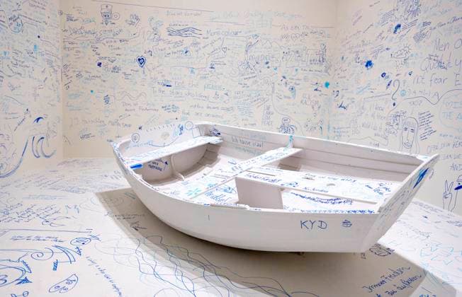 Einzelausstellung Music of the Mind von Yoko Ono in Düsseldorf. Add Colour - Refugee Boat ( Füge Farbe hinzu - Füchtlingsboot ), ein Holzboot, weiß angestrichen, wie auch der gesamte Raum weiß angestrichen ist. Es wird darauf hingewiesen, dass in diesem Raum zu Aufzeichnungszwecken gefilmt wird. Jeder Besucher kann irgendetwas Sinnhaftes oder auch Sinnloses mit Filzstift vermerken. Im Übrigen bezeichnen K20 und K21 der Stiftung Kunstsammlung Nordrhein-Westfalen in Düsseldorf Kunst des 20. und des 21. Jahrhunderts. Bei Yoko Ono ist s beides. Düsseldorf Nordrhein-Westfalen Deutschland