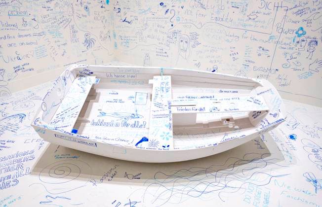 Einzelausstellung Music of the Mind von Yoko Ono in Düsseldorf. Add Colour - Refugee Boat ( Füge Farbe hinzu - Füchtlingsboot ), ein Holzboot, weiß angestrichen, wie auch der gesamte Raum weiß angestrichen ist. Es wird darauf hingewiesen, dass in diesem Raum zu Aufzeichnungszwecken gefilmt wird. Jeder Besucher kann irgendetwas Sinnhaftes oder auch Sinnloses mit Filzstift vermerken. Im Übrigen bezeichnen K20 und K21 der Stiftung Kunstsammlung Nordrhein-Westfalen in Düsseldorf Kunst des 20. und des 21. Jahrhunderts. Bei Yoko Ono ist s beides. Düsseldorf Nordrhein-Westfalen Deutschland