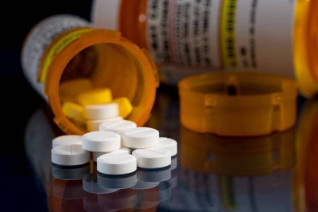 Macro of oxycodone opioid tablets with prescription bottles against dark background Oxycodone is the generic name for a range of opoid pain killing tablets. Prescription bottle for Oxycodone tablets and pills on glass table with reflections Copyright: xZoonar.com StevexHeapx 14108630