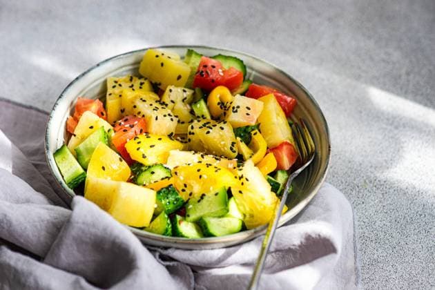 From above a colorful vegetable salad with red and yellow tomatoes, cucumber slices, bell pepper pieces, and sesame seeds in a metal bowl, presented on a gray background. Model Released AnnaBogush_ID24198_701464_003 Copyright: xAnnaxBogushx