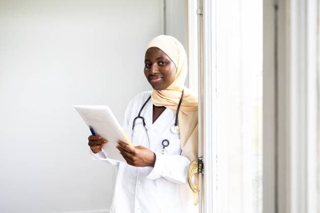 IMAGO Creative, Diversity, Pflege im Krankenhaus Professional black female doctor wearing a hijab and a lab coat, holding a medical file and standing by a window in a well-lit room, reflecting competence and care Model Released DavidMunoz_ID24357_706572_006 Copyright: xDavidxMunozx
