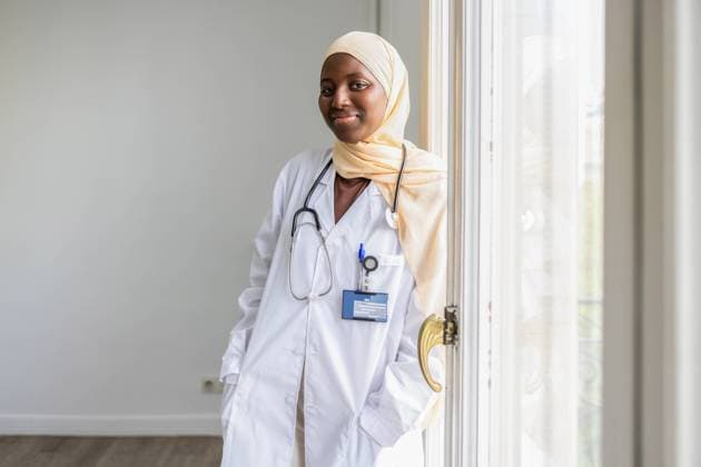 Creative Highlights Symbolfotos A confident female doctor wearing a hijab and white coat stands by a window, representing diversity in healthcare with a smile Model Released DavidMunoz_ID24357_706578_008 Copyright: xDavidxMunozx
