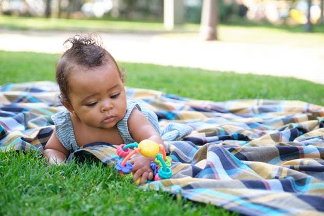 Creative Highlights Symbolfotos A young Mixed race baby girl lies on a colorful blanket in a park, playing attentively with a bright toy Model Released HaruUraraStudio_ID24141_699376_010 Copyright: xHaruxUraraxStudiox RECORD DATE NOT STATED