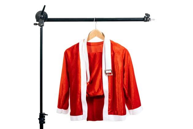 A vibrant red Santa Claus costume with fluffy white trim hanging delicately on a wooden hanger, attached to an adjustable black rack against a stark white background Model Released SergioVictorVega_ID24435_708000_001 Copyright: xSergioxVictorxVegax RECORD DATE NOT STATED