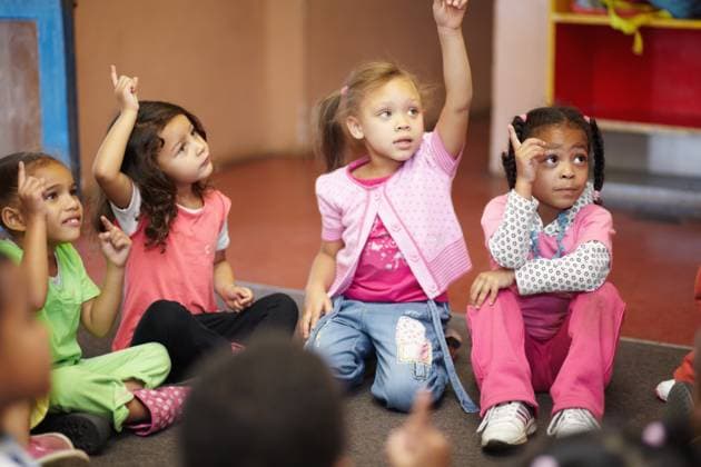 Education, kindergarten and kids asking a question with hands raised while sitting on a classroom floor for child development. School, learning or curiosity with children in class to study for growth. model released property released Copyright: xwww.peopleimages.comx