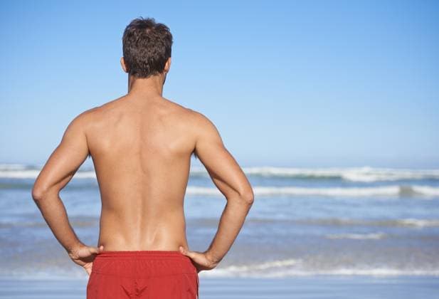 Man, lifeguard and beach for security, emergency or outdoor swimming in health and safety. Rear view or back of male person or professional swimmer stranding ready for patrol at sea or ocean coast. model released property released Copyright: xPeopleImages.comx-x 52b2a9bcd8516x