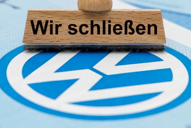 VW-Krise mit Gefahr der Werksschließung Ein Holzstempel ist beschriftet mit dem Aufdruck: Wir schließen, über einer VW-Aktie mit Logo - Symbolbild *** VW crisis with risk of plant closure A wooden stamp is labeled with the words We are closing, above a VW share with logo Symbolic image