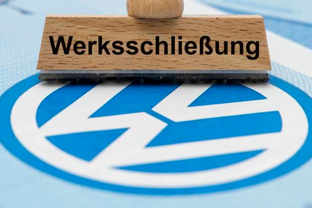 VW-Krise mit Gefahr der Werksschließung Ein Holzstempel ist beschriftet mit dem Aufdruck: Werksschließung, über einer VW-Aktie mit Logo - Symbolbild *** VW crisis with risk of plant closure A wooden stamp is labeled with the words plant closure, above a VW share with logo symbol image