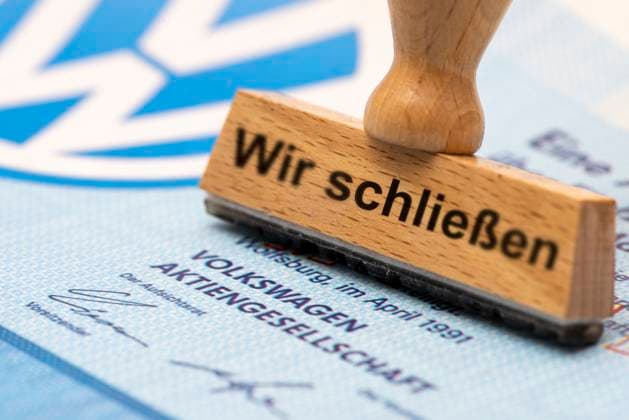 VW-Krise mit Gefahr der Werksschließung Ein Holzstempel ist beschriftet mit dem Aufdruck: Wir schließen, über einer VW-Aktie mit Logo - Symbolbild *** VW crisis with risk of plant closure A wooden stamp is labeled with the words We are closing, above a VW share with logo Symbolic image