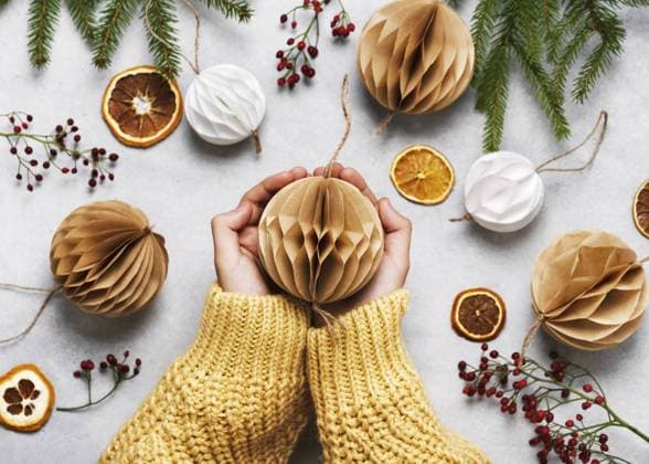 Hände halten eine beige Papierkugel umgeben von weihnachtlichen Dekorationen auf einem Tisch. Handgemachte Honigwaben Bälle aus weißem und braunem Kaffeefilter Papier. Skandinavisches Design Hands holding a beige paper ball surrounded by Christmas decorations on a table. Handmade honeycomb balls made from white and brown coffee filter paper. Scandinavian design Copyright: imageBROKER OksanaxSchmidt ibxoks11555625.jpg